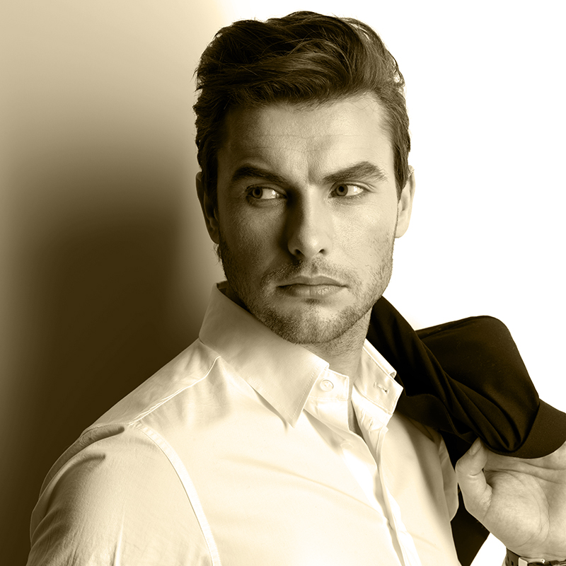 Fashion young man in white shirt holds the black jacket  over wall with contrast shadows